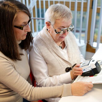 Die Sehhilfenberaterin des BSVH, Marina Sossidi probiert mit einer ratsuchenden Frau eine elektronische Lupe aus