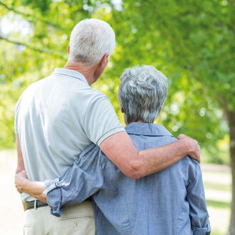 Ein älteres Paar ist von hinten zu sehen. Sie stehen Arm in Arm und betrachten einen Baum