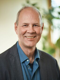 Willy Laudehr trägt ein blaues Hemd, darüber ein dunkles Jacket. Er hat sehr kurzes Haar und lächelt in die Kamera.