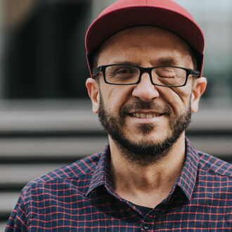 Johannes Mairhofer in Nahaufnahme. Er lächelt in die Kamera. Im Hintergrund erkennt man verschwommen eine Treppe.
