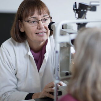 Eine Augenärztin bei der Untersuchung ihrer Patientin. Diese sieht man von hinten.