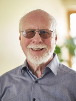 Karsten Warnke im Porträt. Er trägt ein hellblaues Oberhemd und eine getönte Brille. Er lächelt in die Kamera.