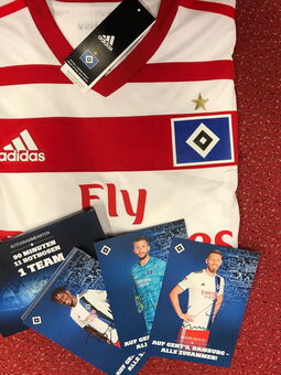 Das Trikot des HSV gefaltet. Darüber liegt eine Box mit Autogrammkarten aller Spieler der Saison 2019/2020