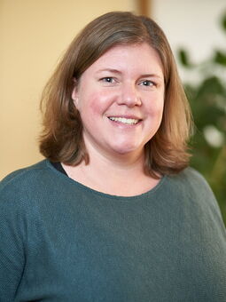 Cora Kelma im Porträt. Sie trägt einen grünen Pullover mit Rundhals-Ausschnitt. Ihr Haar ist mittelblond uns fällt ihr leicht auf die Schultern. Sie lächelt freunldich in die Kamera.