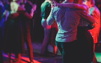 Mehrere Tanzpaare bewegen sich im rötlichen Discolicht