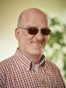 Axel Fandrey trägt eine dunkel getönte Brille und lächelt in die Kamera. Gekleidet ist er mit einem karierten Hemd.