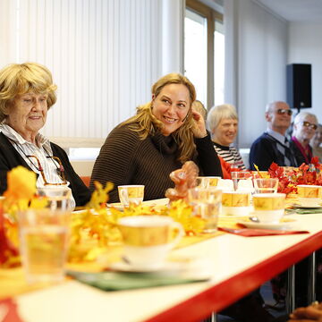 Die Seniorenberaterin des BSVH, Franziska Diesmann eingerahmt von Teilnehmern und Teilnehmerinnen ihres Seniorennachmittags. Alle sitzen an einem langen gedeckten Kaffeetisch.