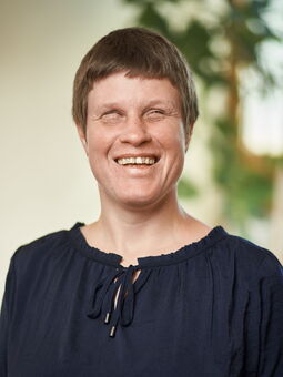Katja Löffler hat kurzes braunes Haar und lächelt in die Kamera. Sie trägt eine dunkelblaue Bluse mit Schleife.