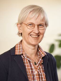 Angelika Antefuhr lächelt in die Kamera. Sie trägt ihr weißes Haar kurzgeschnitten und eine hellbraune, runde Brille. Gekleidet ist sie mit einer karierten Bluse und einem dunkelblauen Blazer. Um ihren hals eine Silberkette mit einem blauen Anhänger.