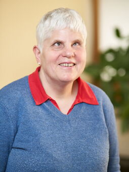 Dagmar Holtmann trägt ihr weißes Haar kurzgeschnitten. Sie lächelt in die Kamera. Gekleidet ist sie mit einem roten Poloshirt und einem hellblauen Pullover.