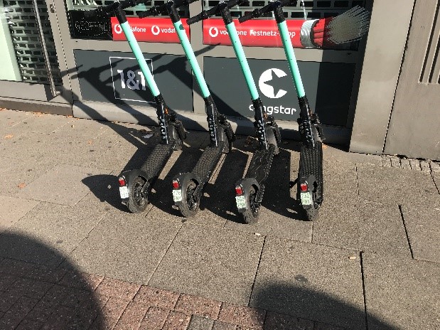 E-Scooter wurden vom Verleiher vor einem Geschäft so aufgereiht, dass sie in den Fußweg hineinragen.