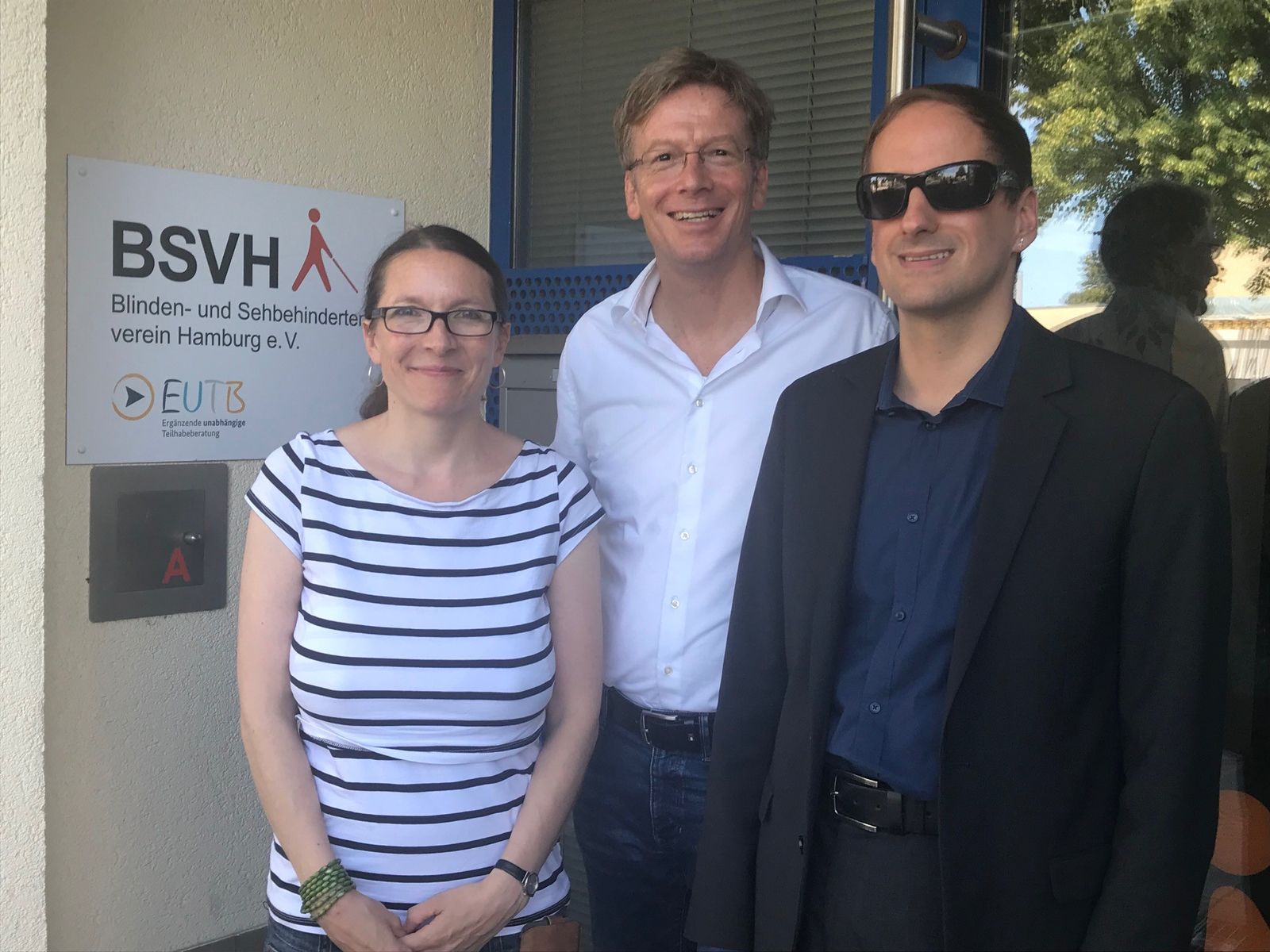 Vor dem Eingangsschild des Louis-Braille-Centers, auf dem steht: BSVH/EUTB-Beratung stehen (v.l.): Ksenia Bekeris und Dirk Kienscherf (SPD-Bürgerschaftsfraktion) und Heiko Kunert, Geschäftsführer des BSVH